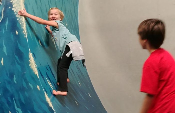 Day camp student making it partway up the warped wall, looking back towards the camera